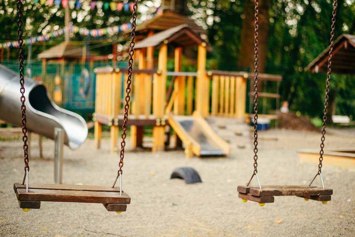 Empty playground showing wooden swings and play structure in the early evening. Kind of spooky feeling to it.