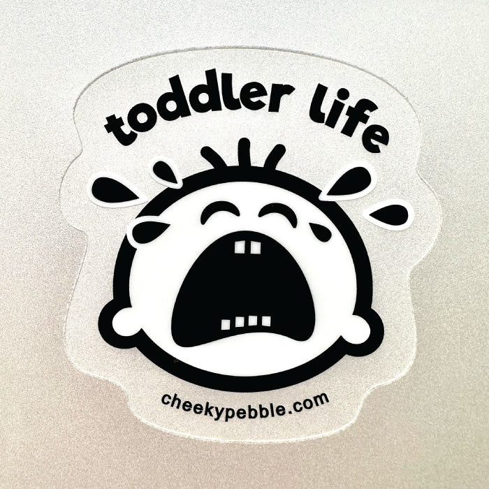 Toddler Life Clear Sticker by Cheeky Pebble shown on a silver laptop. Our Cheeky crying toddler face is a clear sticker with solid white background behind the face and tears.