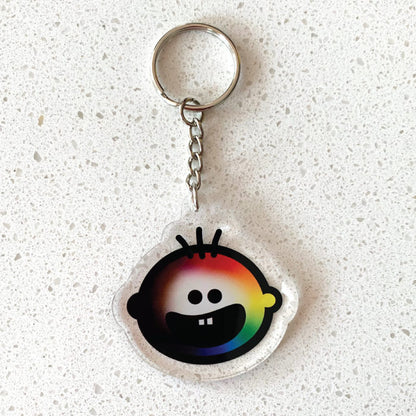 Our ‘Love for all’ charm featuring a rainbow Cheeky Pebble face on a silver keychain and ring. Displayed on a quartz background..